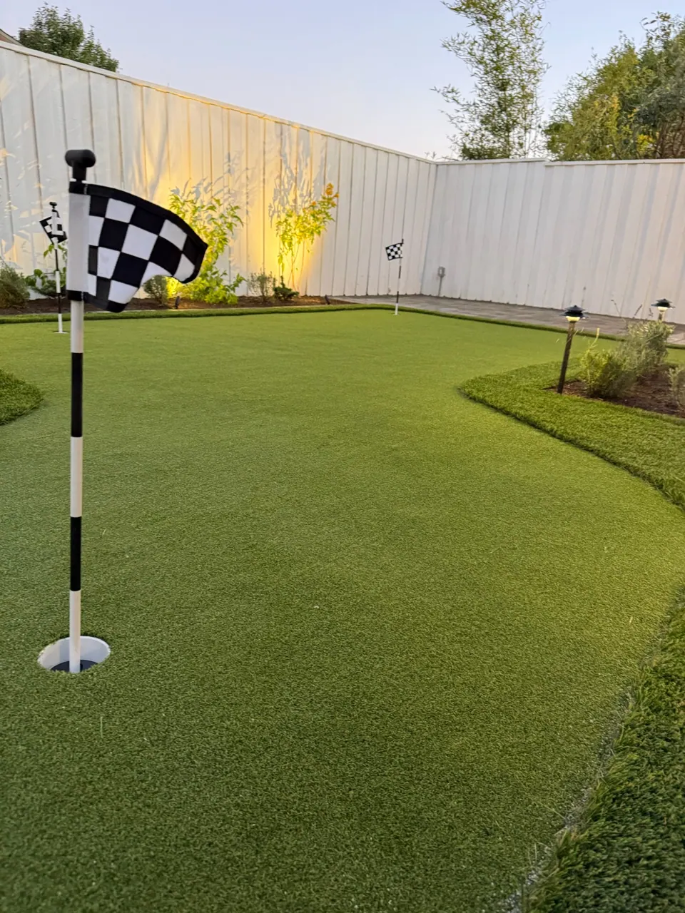 A putting green flag beside an uplit planting bed at dusk
