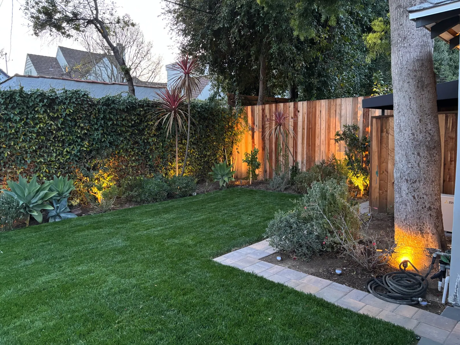 Lawn and planting with warm uplights on a wood fence at dusk