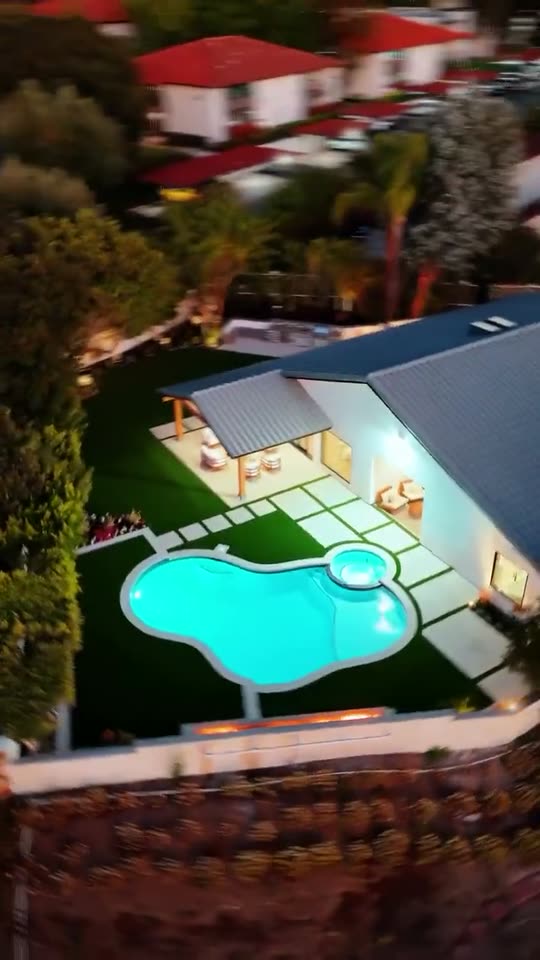 A finished pool and lawn behind a house, seen from above at dusk