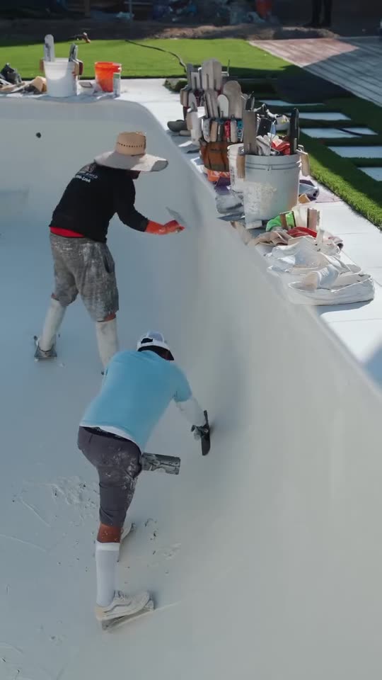 A crew troweling white plaster inside an empty pool